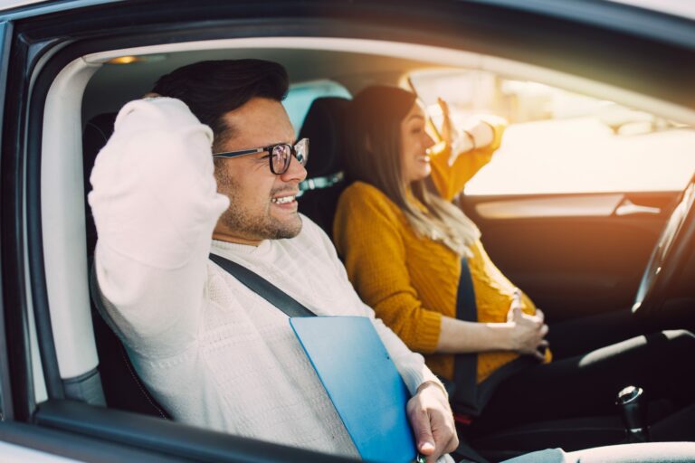 Driving school or test. Beautiful young pregnant woman learning how to drive car together with her instructor.