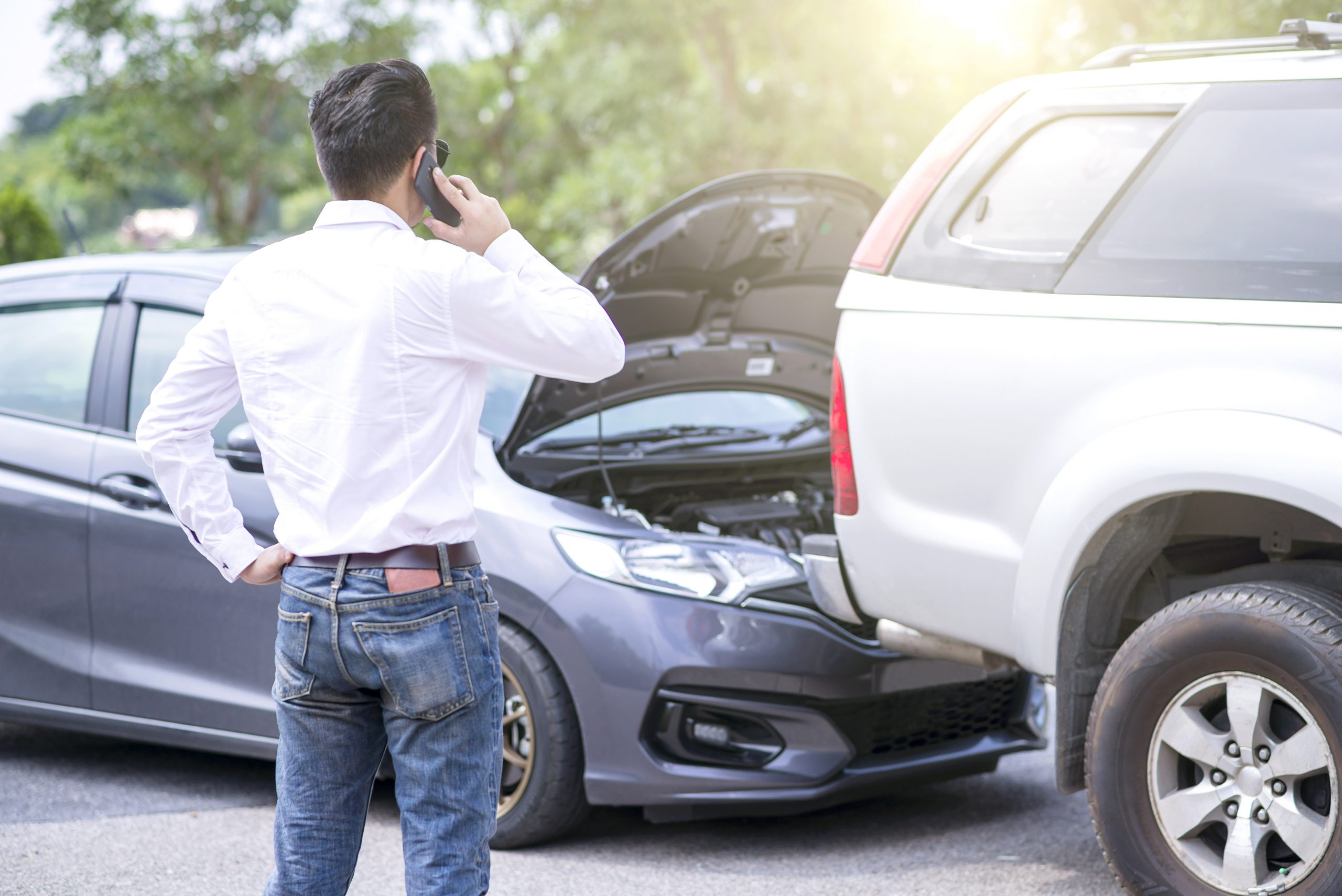The driver is calling for insurance after a traffic accident. car crash accident on street, damaged automobiles after collision. The car crashed on a road between a saloon and a pickup.