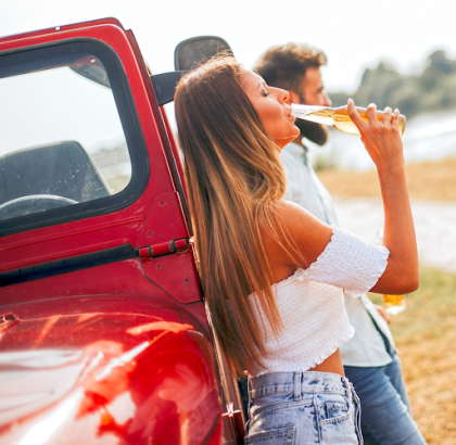 Passenger drinking alcohol beside a vehicle before a potential DUI accident
