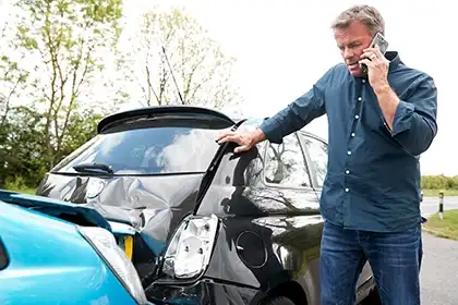 Driver calling for help beside a damaged car after an auto accident