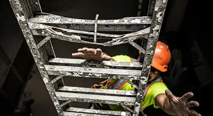 A construction worker climbing up a damaged ladder without proper support