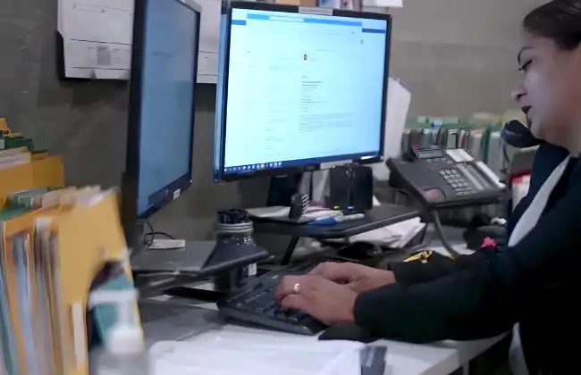 AK Law staff member works at a dual-monitor computer setup while speaking on the phone, surrounded by case files and office documents