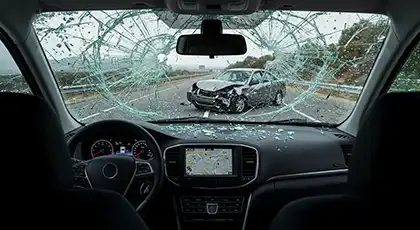 View from inside a car after a crash, with a shattered windshield and another damaged vehicle ahead