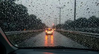 View through rainy windshield showing taillights on wet road