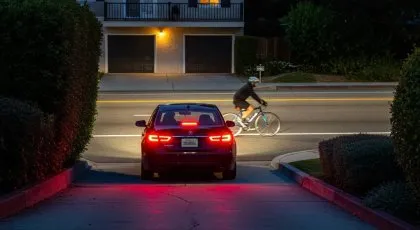 Car exiting driveway at night as cyclist passes on the road