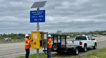 Highway workers inspecting a solar-powered call box in San Diego County