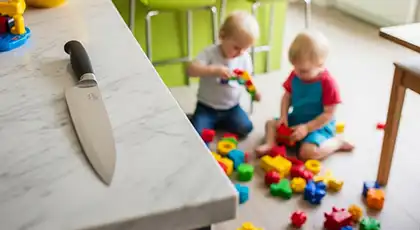 Large kitchen knife resting near the edge of a marble countertop, with two young children playing on the floor