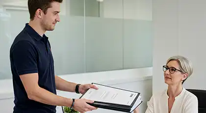 Man handing over a stack of documents to a seated woman in an office