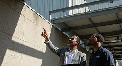 Two men inspect a building exterior with one pointing upward