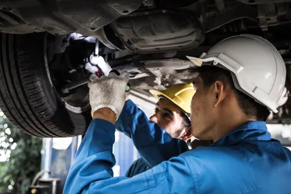 Mechanics inspecting vehicle undercarriage after a collision to assess alignment damage