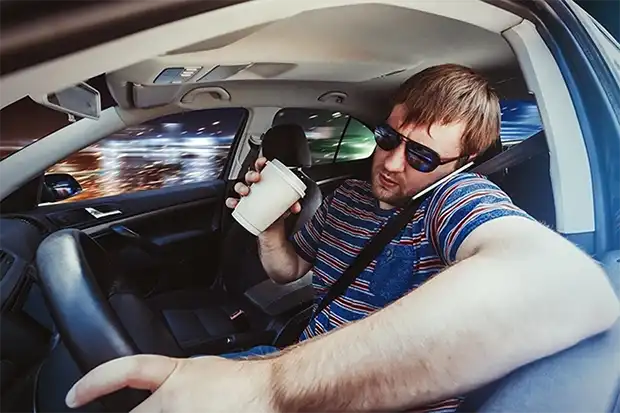 Reckless driver multitasking behind the wheel with a drink and phone