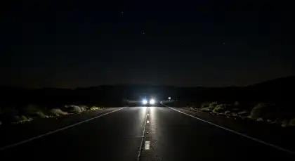 Car using high beams on a dark rural road at night