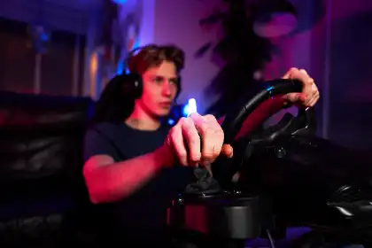 Teen playing a racing video game with a steering wheel controller