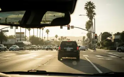View through a car windshield showing vehicles stopped at a California intersection under a traffic light