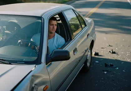 Man sitting in damaged car after traffic accident with debris on roadway