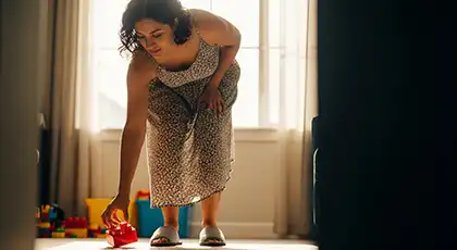 Mujer agachándose para recoger un juguete rojo del suelo en un suave