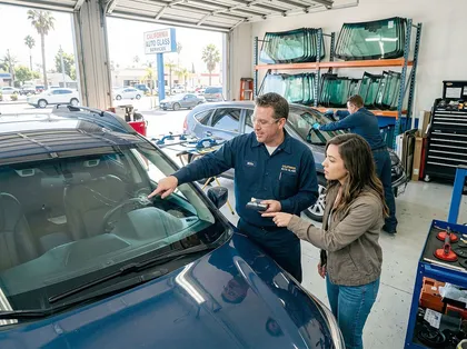 auto technician inspecting cracked windshield damage with driver
