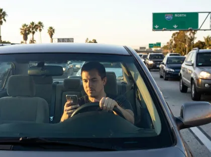 Distracted driving scene showing motorist texting in car on crowded highway with vehicles surrounding him