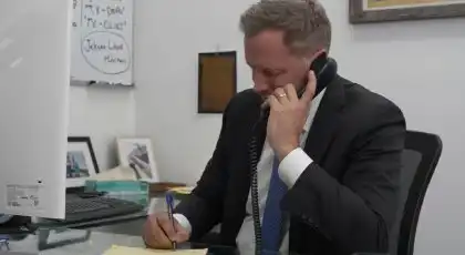 Un abogado de AK hablando por teléfono y tomando notas en un escritorio, prestando asistencia en una reclamación por accidente de tráfico sin informe policial