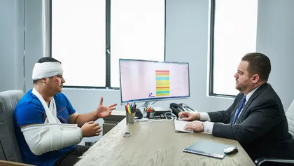 Un hombre lesionado, con vendajes, está consultando a un abogado especializado en lesiones personales en el despacho