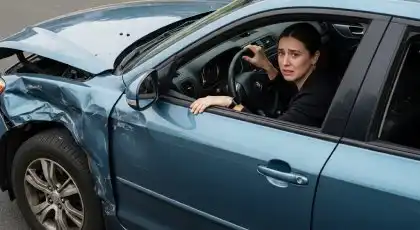 Una mujer angustiada en un coche accidentado tras un choque, sin saber si debe denunciarlo