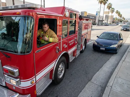 Camión de bomberos en una calle de la ciudad con un bombero dentro mirando su móvil, mientras pasan coches