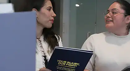 Dos mujeres en una oficina sosteniendo una carpeta mientras mantienen una conversación