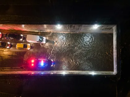Inundación provocada por una tormenta en un paso subterráneo de la autopista por la noche, captada desde una perspectiva aérea, con los coches parcialmente parados y la policía controlando la situación
