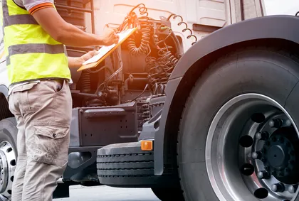 Mechanic inspecting a large truck engine while holding a clipboard and taking notes