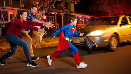 Niño disfrazado que sale corriendo a la calle mientras sus padres se lanzan a detenerlo para evitar que lo atropelle un coche que se aproxima