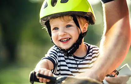 Niño sonriente con casco de bicicleta siendo sostenido por un adulto mientras aprende a montar