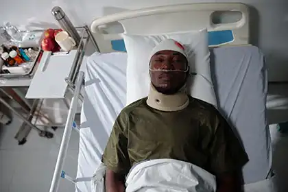 Paciente en cama de hospital con collarín y lesión en la cabeza