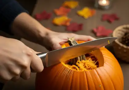 Persona que utiliza un cuchillo de cocina grande para tallar la parte superior de una calabaza, lo que ilustra el riesgo de sufrir accidentes al tallar