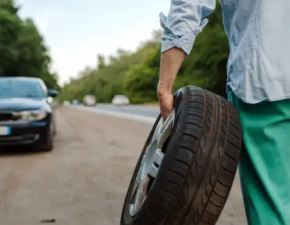 Persona sosteniendo una llanta junto a auto averiado en carretera