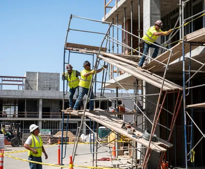Trabajadores en una obra de construcción que fijan un andamio un trabajador sube por él mientras los demás lo sujetan para mantenerlo estable