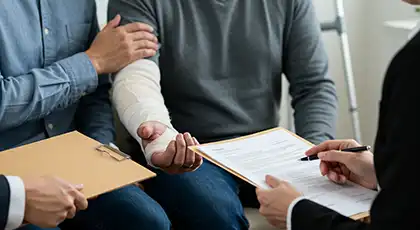 Tres personas que revisan documentos legales; una de ellas tiene un brazo vendado, lo que simboliza la responsabilidad civil y la indemnización tras un accidente en un drive-thru.