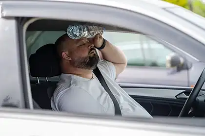 Un conductor con sobrepeso y cansado que se refresca la cabeza con una botella de agua