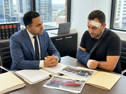 Abogado que comenta un caso de accidente automovilístico con un hombre lesionado —que lleva un vendaje en la cabeza y un soporte para el brazo— durante una consulta legal sobre lesiones personales.