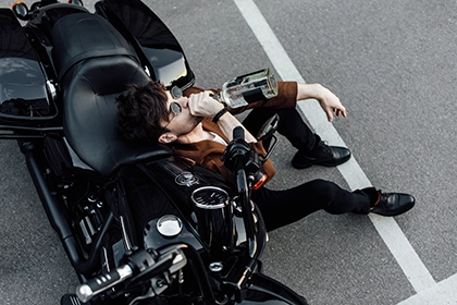 hombre bebiendo alcohol junto a su moto