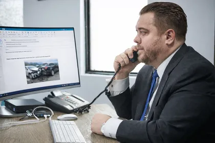 Abogado especializado en lesiones personales hablando por teléfono mientras revisa las pruebas de un accidente en su escritorio de la oficina