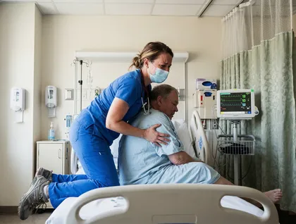 Enfermera que levanta a un paciente de una cama de hospital, lo que ilustra la realización de levantamientos repetitivos en el trabajo