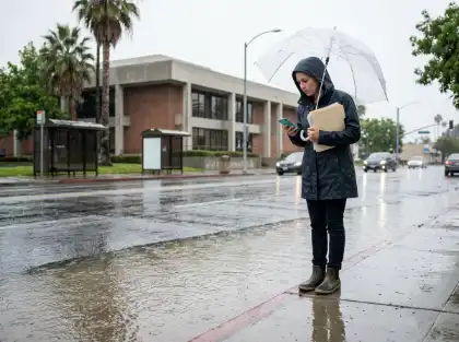 Mujer mirando el móvil bajo un paraguas junto a una calle inundada de California