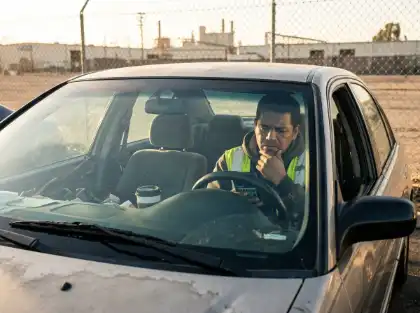 Construction worker reviewing information on a smartphone while sitting inside a parked car