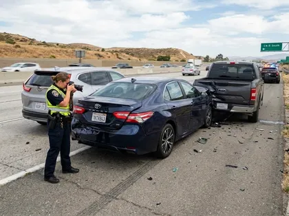Highway crash scene with a police officer documenting vehicle damage and debris after a multi-car collision