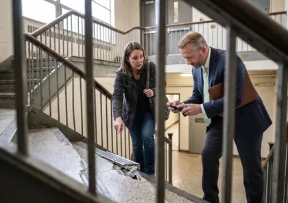 Abogado especializado en lesiones escolares inspeccionando una escalera peligrosa mientras evalúa una reclamación por lesiones de un alumno