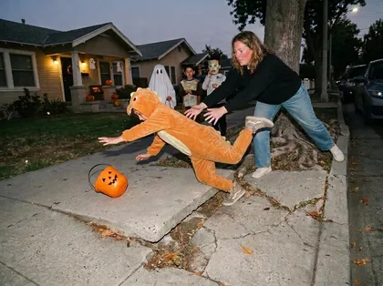 Child in a Halloween costume tripping on a broken public sidewalk while trick-or-treating in California