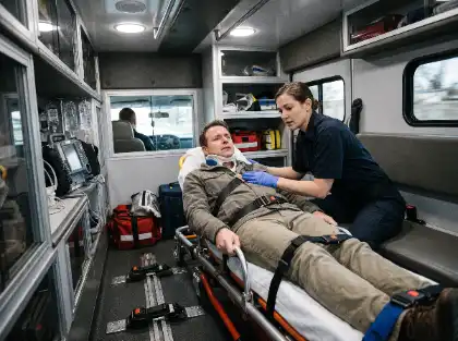 Paramedic assisting an injured patient on a stretcher inside an ambulance