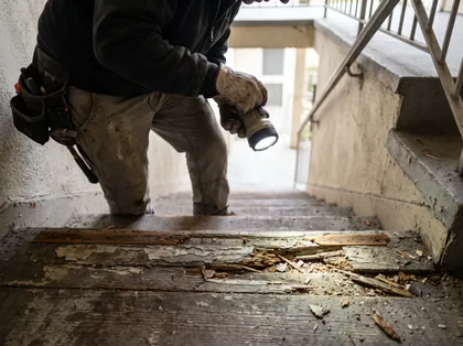 Trabajador que inspecciona unas escaleras dañadas en busca de riesgos relacionados con la responsabilidad civil de los locales