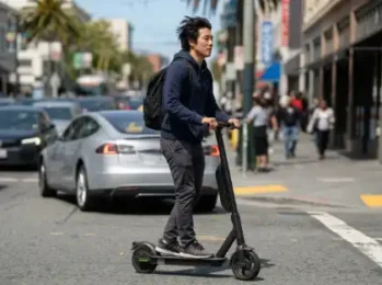 Un hombre con una mochila que circula en un patinete eléctrico sin casco por una calle muy transitada de la ciudad